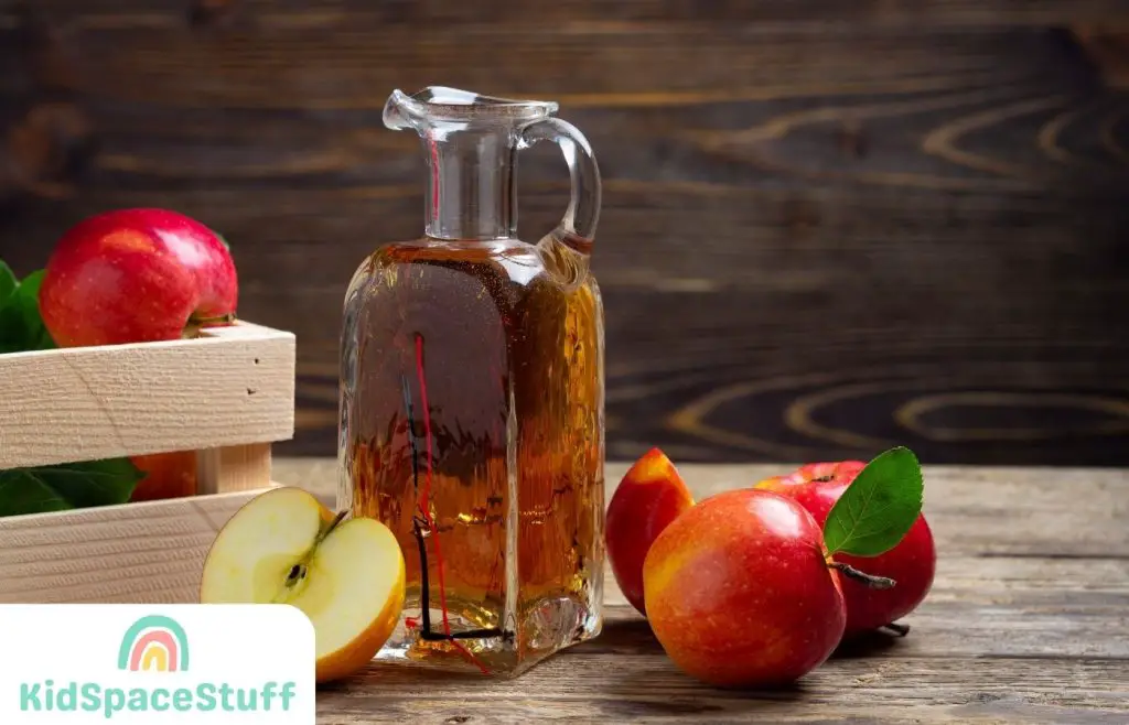 A picture of apple cider vinegar beside an apple fruit